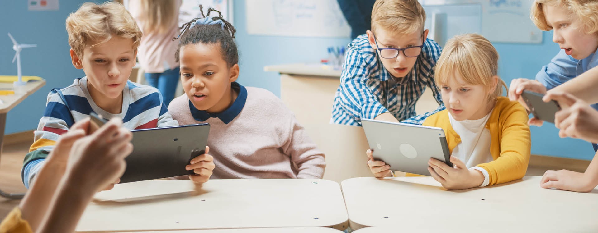 Kinder in einem Klassenraum nutzen unterschiedliche digitale Endgeräte.