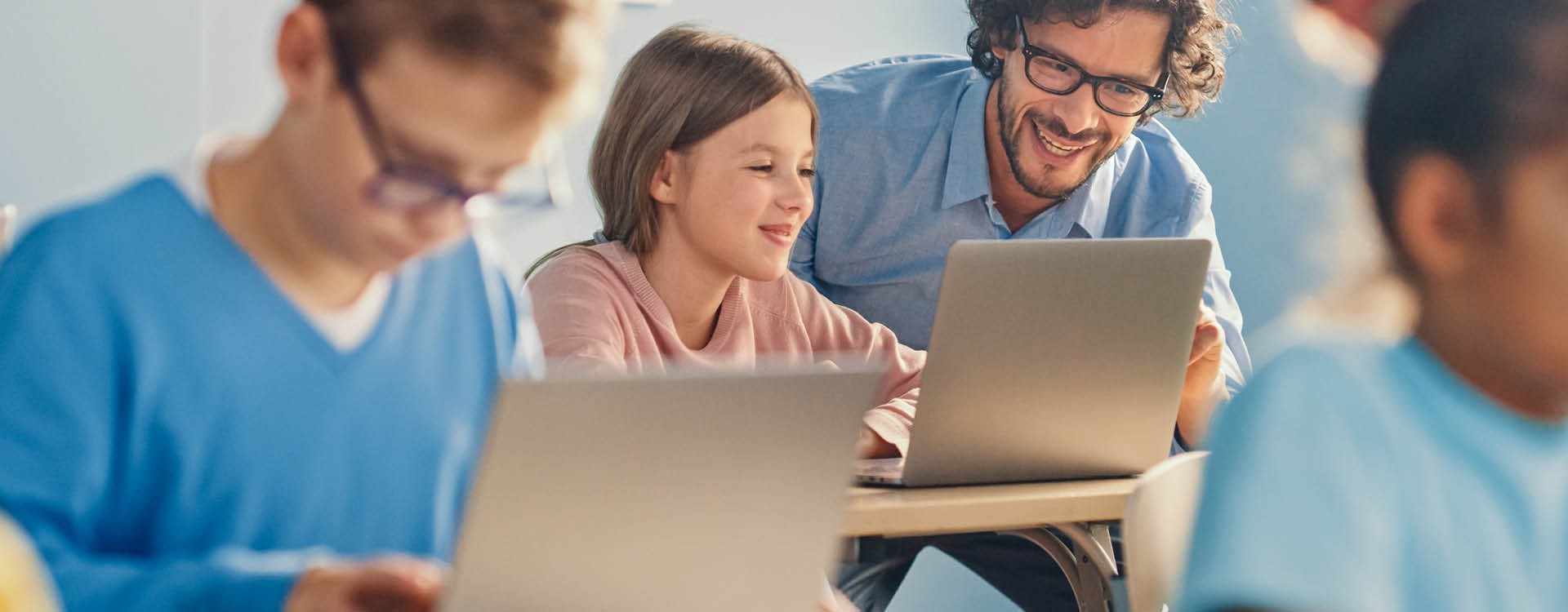 Lehrer berät eine Schülerin, die am Laptop sitzt.