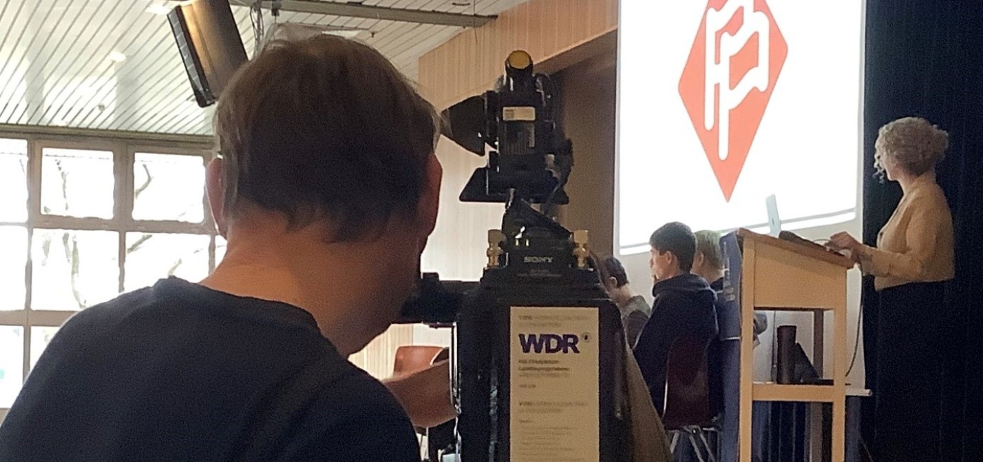 Eine Gruppe Jugendlicher spielt das Edu-LARP Europe Alive. Die Personen stehen auf der Bühne und debattieren. Ein Kameramann des WDR filmt die Situation.