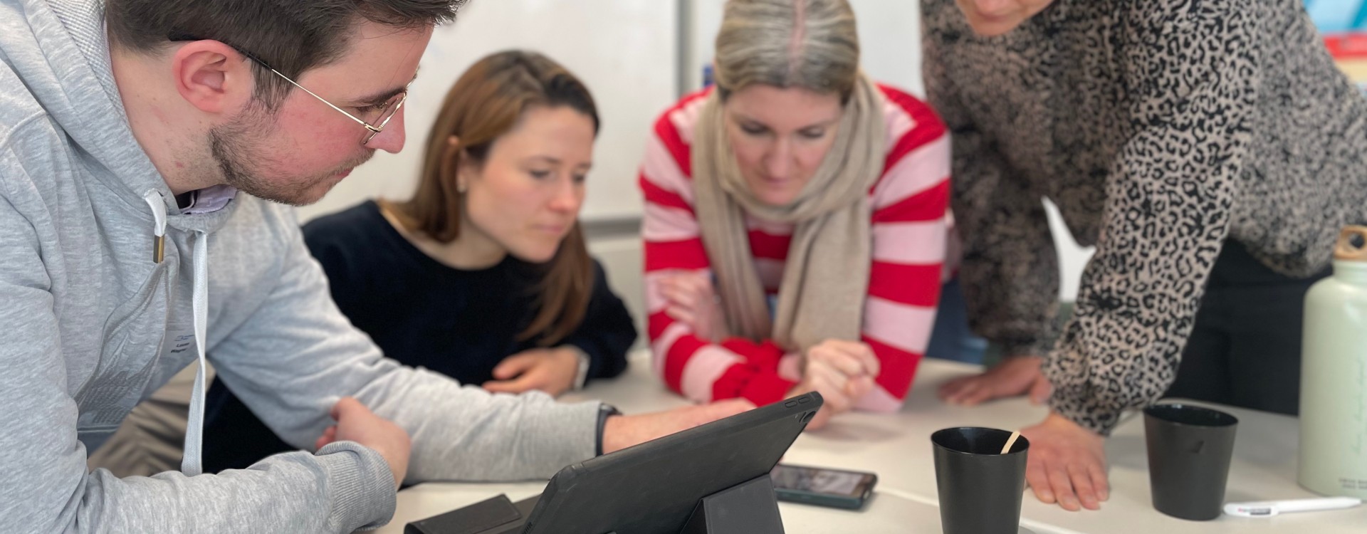 Vier Lehrkräfte blicken während einer Arbeitsphase gemeinsam auf ein Smartphone.