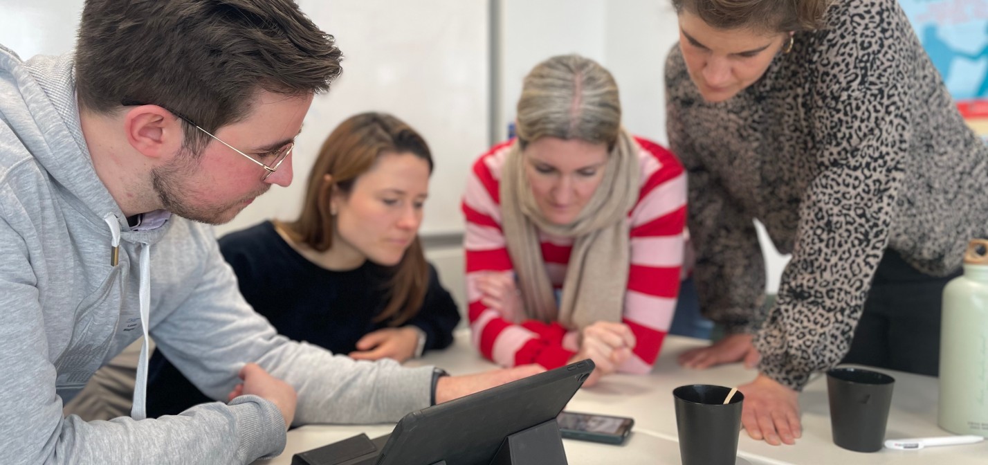 Vier Lehrkräfte blicken während einer Arbeitsphase gemeinsam auf ein Smartphone.